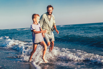 Happy father and son, man & boy child, running and having fun in the sand and waves of a sunny beach