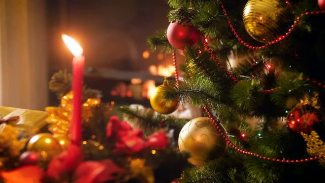 Closeup 4k video of glowing lights on decorated Christmas tree, candle and burning fireplace. Perfect background for winter celebrations and holidays
