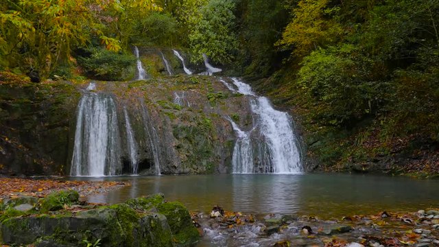 Picturesque forest stage waterfall with a small lakelet dressed in autumn colors 4K