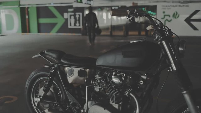 Biker guy walking through the parking from his motorcycle. Motorcyclist and vintage motorbike from 1970s in the garage. Side view urban lifestyle scene. Slow motion video shooting by handheld gimbal