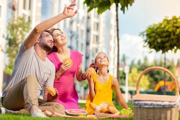Look there. Nice happy man pointing at the sky while sitting together with his family
