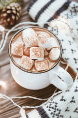 Hot cocoa with marshmallow in a white ceramic mug surrounded by winter things on a wooden table. The concept of cosy holidays and New Year.