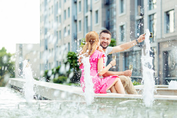 Love and romance. Joyful happy couple enjoying their romantic date while sitting near the fountain with champagne