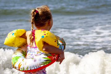 Happy little girl with floaties floaties preparing to swim in the ocean