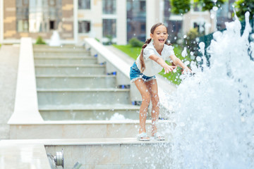 Great mood. Happy positive girl looking at the water from the fountain while stretching her hands to it