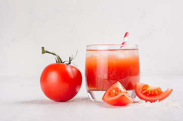 Red tomato cocktail in misted glass with juicy slice cut tomato, straw, ice, salt on soft white wood board, copy space.