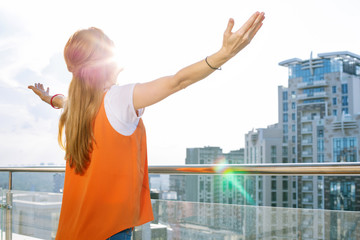 Feeling of freedom. Happy nice woman looking at the sun while standing on the balcony