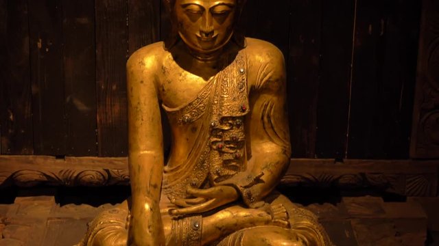 Tilt up shot of a golden Buddha sitting in a wooden lodge.