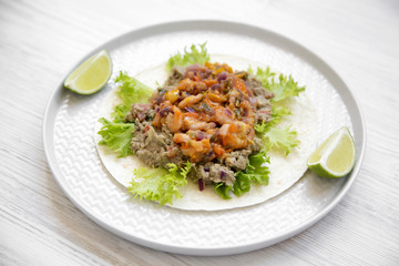 Shrimp taco with lime on round plate over white wooden surface, side view. Close-up.