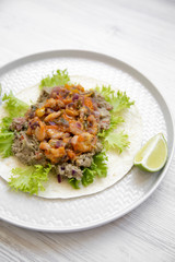 Shrimp taco with lime on round plate on white wooden table, side view. Mexican cuisine.