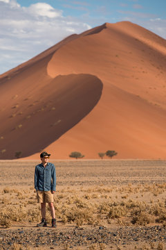 Young male traveler standing in Namib desert with orange sand dune in the background. Travel Namibia, Africa concept