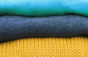 Stack of multicolored and trend Ceylon yellow woolen knitted sweaters close-up, texture, background