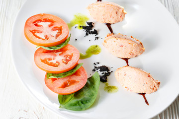 Caprese salad with mozzarella, tomato, basil and balsamic vinegar arranged on white plate