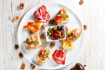 Plate with Italian appetizers. Bruschetta with a cherry tomatoes and shrimps. Parmesan cheese, prosciutto, green capers, olives, sun-dried tomatoes and walnuts.