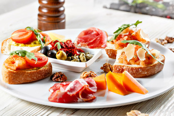 Plate with Italian appetizers. Bruschetta with a cherry tomatoes and shrimps. Parmesan cheese, prosciutto, green capers, olives, sun-dried tomatoes and walnuts.