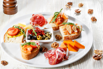 Plate with Italian appetizers. Bruschetta with a cherry tomatoes and shrimps. Parmesan cheese, prosciutto, green capers, olives, sun-dried tomatoes and walnuts.
