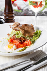 Classical Caesar salad with roasted chicken, poached egg, lettuce leaves, crackers, parmesan and tomatoes and cream sause on the white round plate close up. restaurant menu