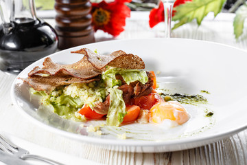 Classical Caesar salad with roasted chicken, poached egg, lettuce leaves, crackers, parmesan and tomatoes and cream sause on the white round plate close up. restaurant menu