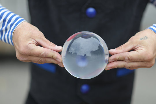 Transparent magic ball with reflection in the hands of a clown