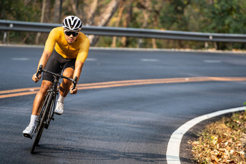 Focus on Asian man wearing a yellow cycling jersey, who's riding a road bike up high on hill in the morning. Under morning sunshine with determination on his face.