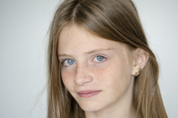 Beautiful blond young girl with freckles indoors on white wall background, closeup portrait