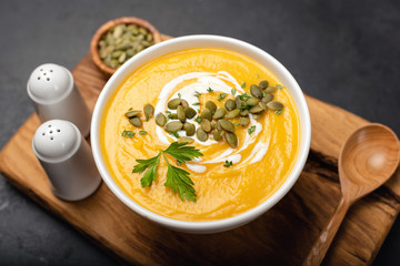 Pumpkin cream soup topped with cream and pumpkin seeds on serving board. Closeup view, selective focus