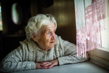 Gray-haired elderly woman sits and looks out the window.