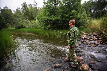  Fisherman standing on stones catching fish on the river.