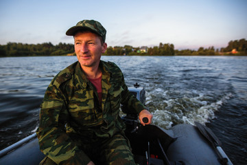 Obraz premium Portrait of a man in camouflage driving a motor boat in sunset time.