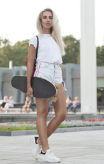 Portrait of smiling young female skateboarder holding her skateboard. Woman with skating board at skate park looking at camera outdoors.