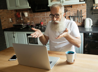 Horizontal shot of frustrated senior Caucasian male employee with gray beard and eyewear holding hands on his bald head, having panic look, feeling stressed because of deadline. Age and job