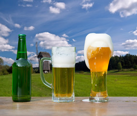 Pouring glass of beer from bottle on landscape background