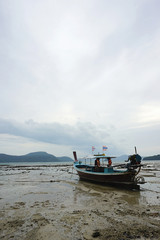 Fototapeta na wymiar Fisherman boat parking on the lower tide beach with the dull sky background