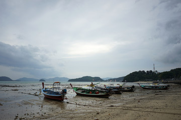 Fisherman boat parking on the lower tide beach with the dull sky background