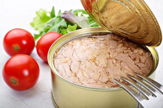Canned tuna in olive oil with tomatoes and salad on white plaster background