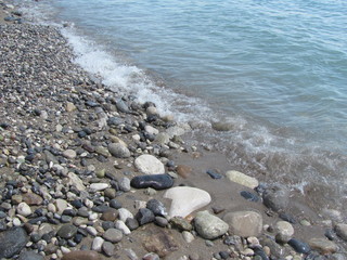 The shore of the sea close-up: a pebble from a pebble with sand and an incident wave. Beautiful background.