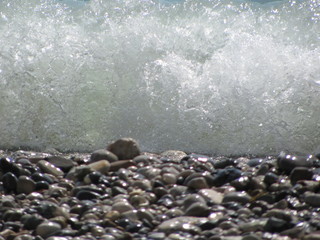 Fototapeta premium The shore of the sea close-up: a pebble from a pebble with sand and an incident wave. Beautiful background.