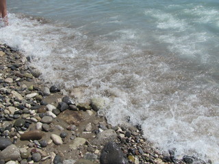 The shore of the sea close-up: a pebble from a pebble with sand and an incident wave. Beautiful background.