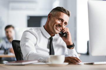 Image of european adult man 30s wearing white shirt and tie sitting at desk in office by computer,...
