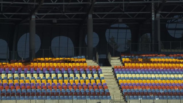 Football stadium with empty tribunes. Empty different colors seats in sports stadium. Section of plastic chairs on grandstand. Modern open olympic arena at daylight. Soccer stadium fans zone