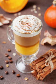 Pumpkin spiced latte or coffee in glass on brown background. Autumn, fall or winter hot drink.