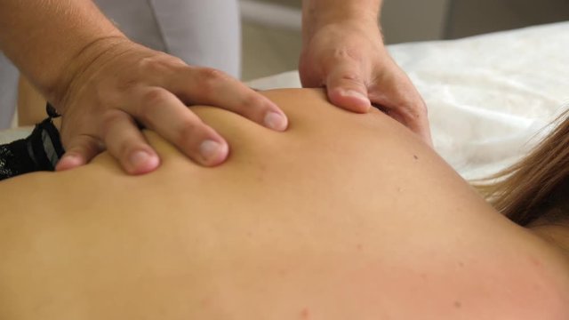 Manual therapist massaging a young woman lying on a massage table, pushing on the back. Male masseur hands massaging beautiful woman back in spa closeup.