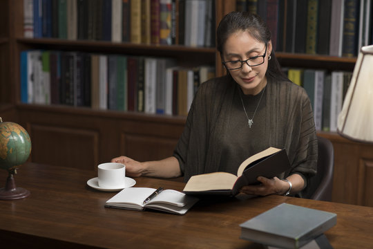Elegant mature woman reading book in study