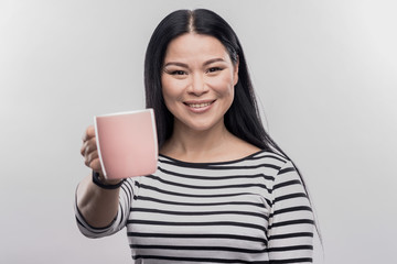 Cup with coffee. Smiling appealing businesswoman holding pink cup with hot coffee on image without...