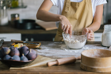 cropped shot of woman in apron mixing dough for pie with spoon on rustic wooden table