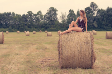 Naklejka na ściany i meble Beautiful woman sitting on hay bale a summer's day