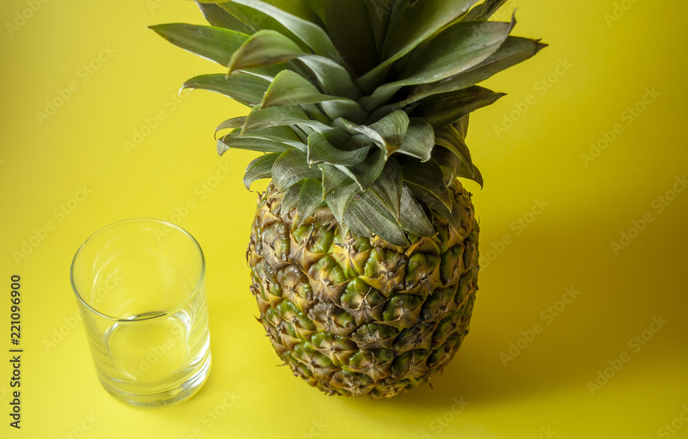 Wall mural single pineapple isolated on yellow background with empty glass.