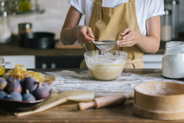 cropped shot of woman spilling flour into bowl with sieve during pie preparation
