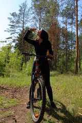 brunette girl on a bike in the woods drinking water from a bottle