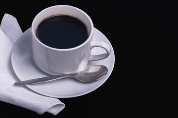 a cup of black coffee on a saucer and a cloth napkin on a dark background